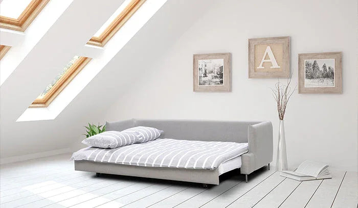 Como-vuodesohva pedattuna kaltevakattoisessa huoneessa jossa isot kattoikkunat.