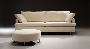HT Collectionin Clara-sohva ja pyöreä rahi valkoisella kankaalla. 